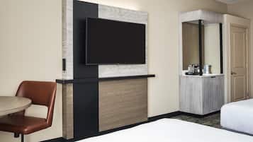 A hotel room with a flat-screen TV mounted on a wall, a wooden cabinet with a mirror, a brown leather chair, and a bed.