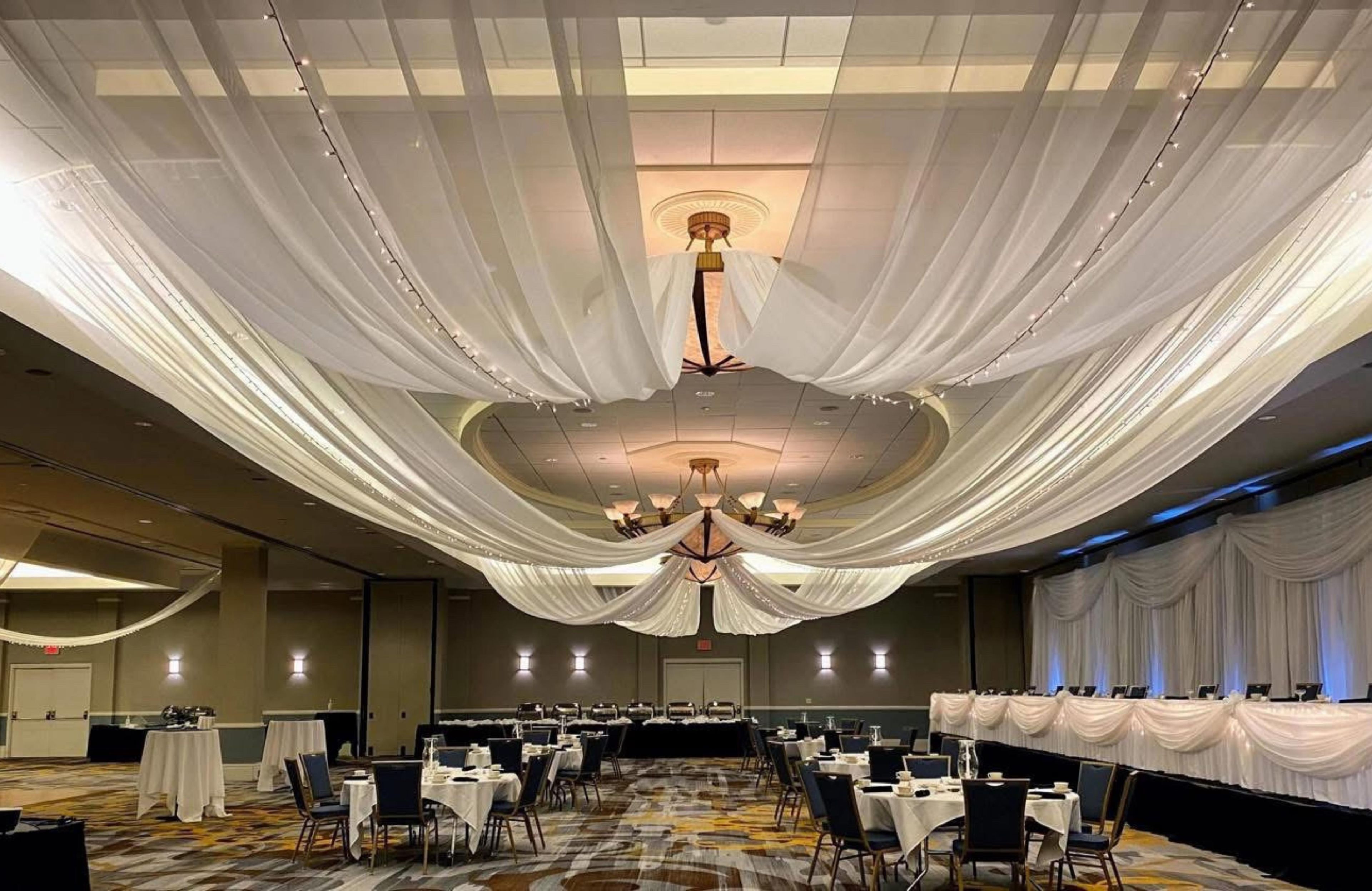 A banquet hall with tables arranged for dining, a chandelier, and draped fabric on the ceiling.