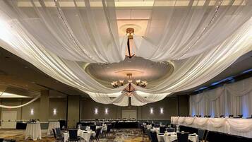 A banquet hall with tables arranged for dining, a chandelier, and draped fabric on the ceiling.