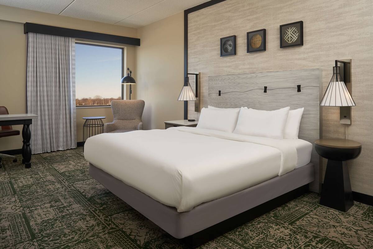 A hotel room with a large bed, a desk, a chair, and a view of the city.
