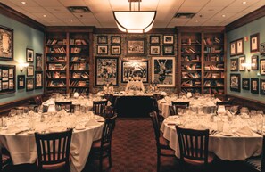 A formal dining room with multiple tables set for service, surrounded by bookshelves and framed pictures on the walls. - Hilton Appleton Paper Valley (Appleton)