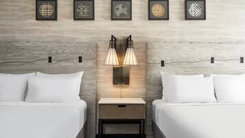 Habitación de hotel con dos camas, una mesita de noche, una lámpara de pared y cinco cuadros enmarcados.