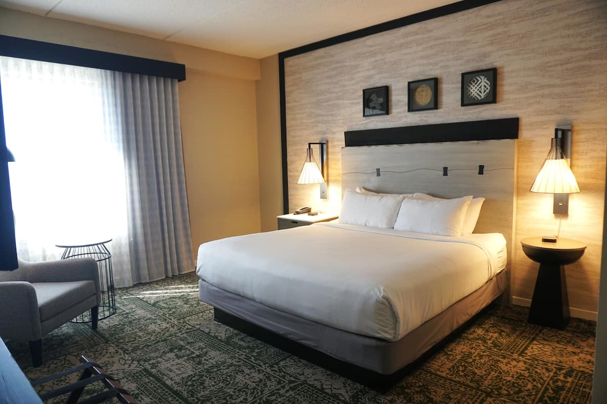 A hotel room with a large bed, two bedside lamps, a nightstand, a chair, and a patterned carpet.