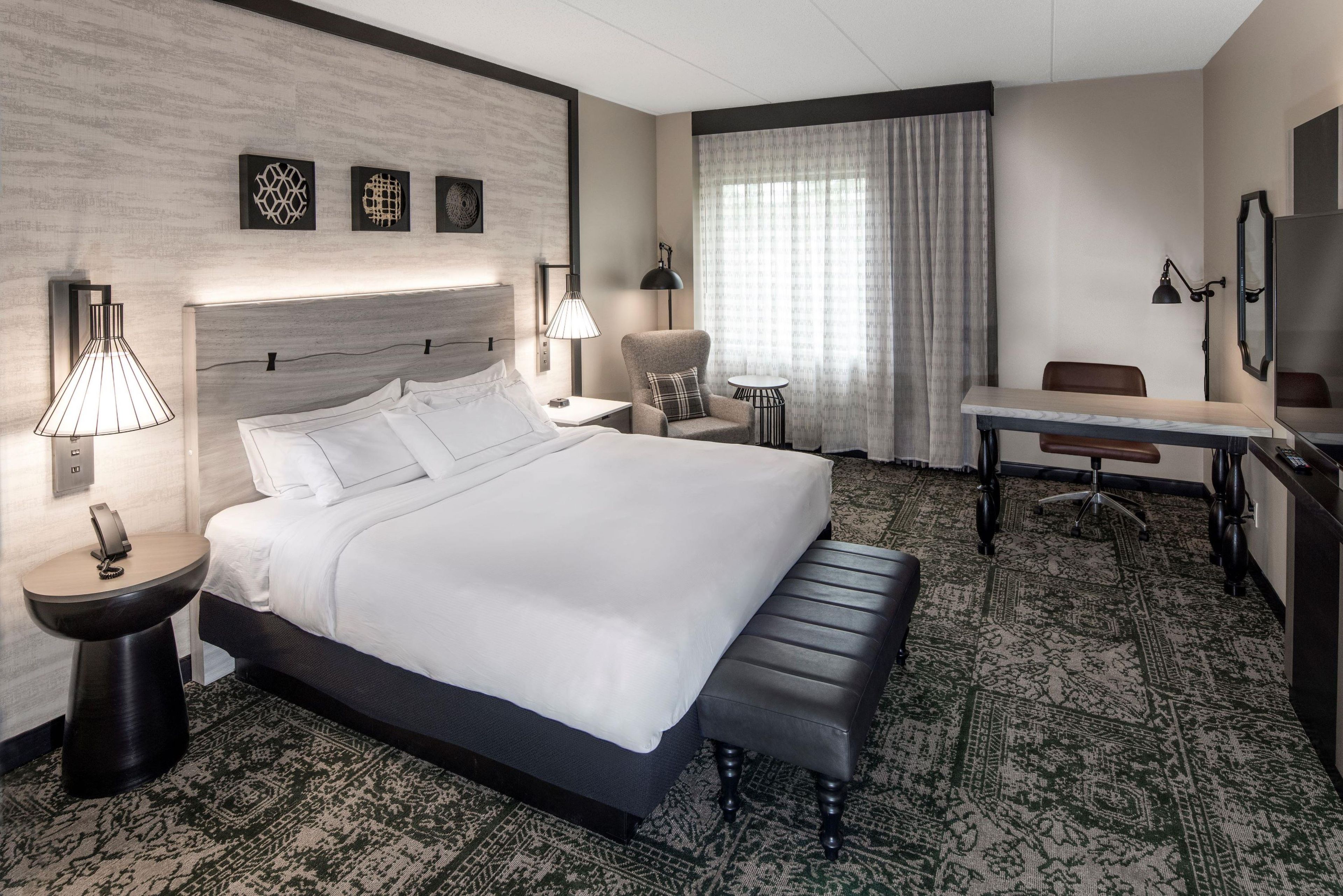 Ein Hotelzimmer mit einem großen Bett, Nachttischlampen, einem Schreibtisch und einem Sessel.