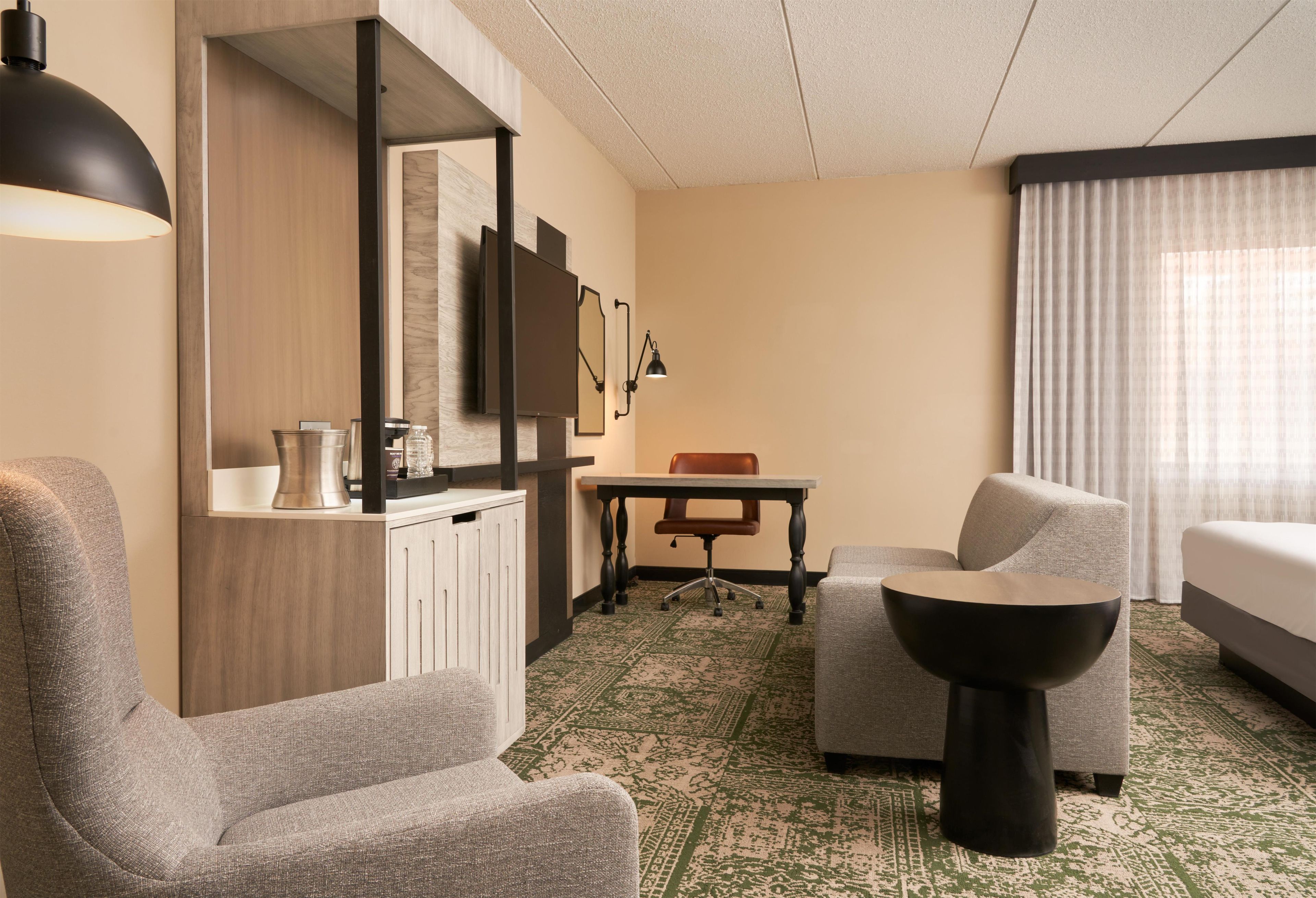 A hotel room with a sofa, a chair, a small table, a coffee machine, a mirror, and a TV.