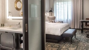 A hotel room with a large bed, a separate bathroom with a vanity, a desk, and a patterned rug. - Hilton Appleton Paper Valley (Appleton)
