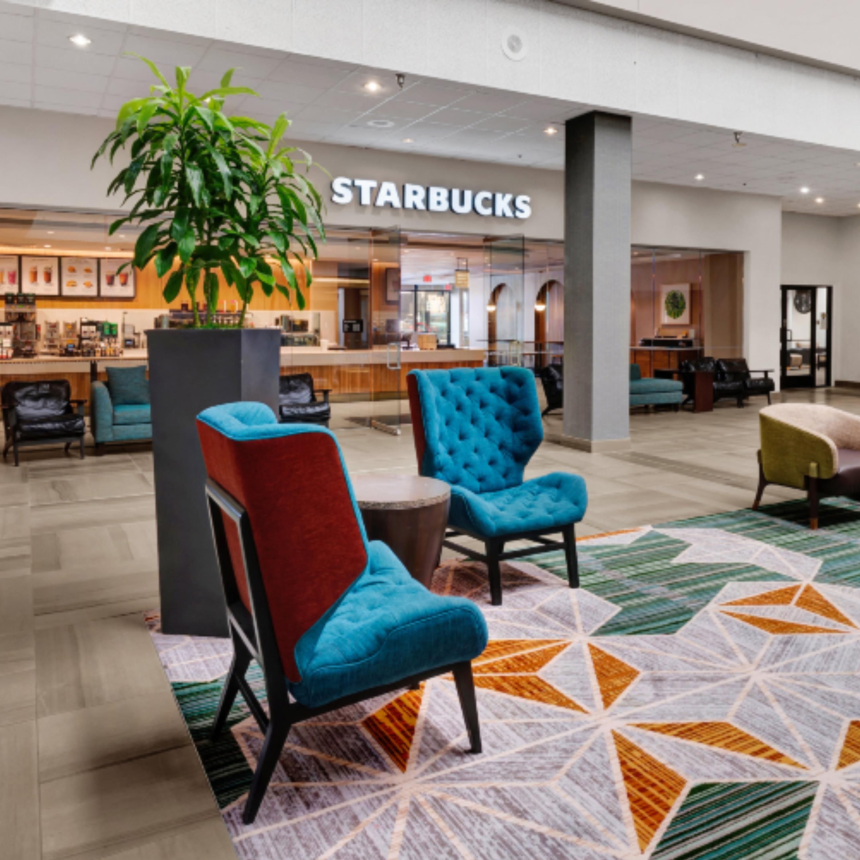 A Starbucks in a modern lobby with seating areas and a large plant.