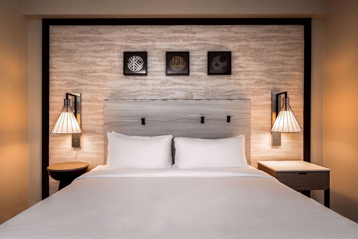 A hotel room with a large bed, two bedside tables with lamps, and three framed artworks on the headboard.