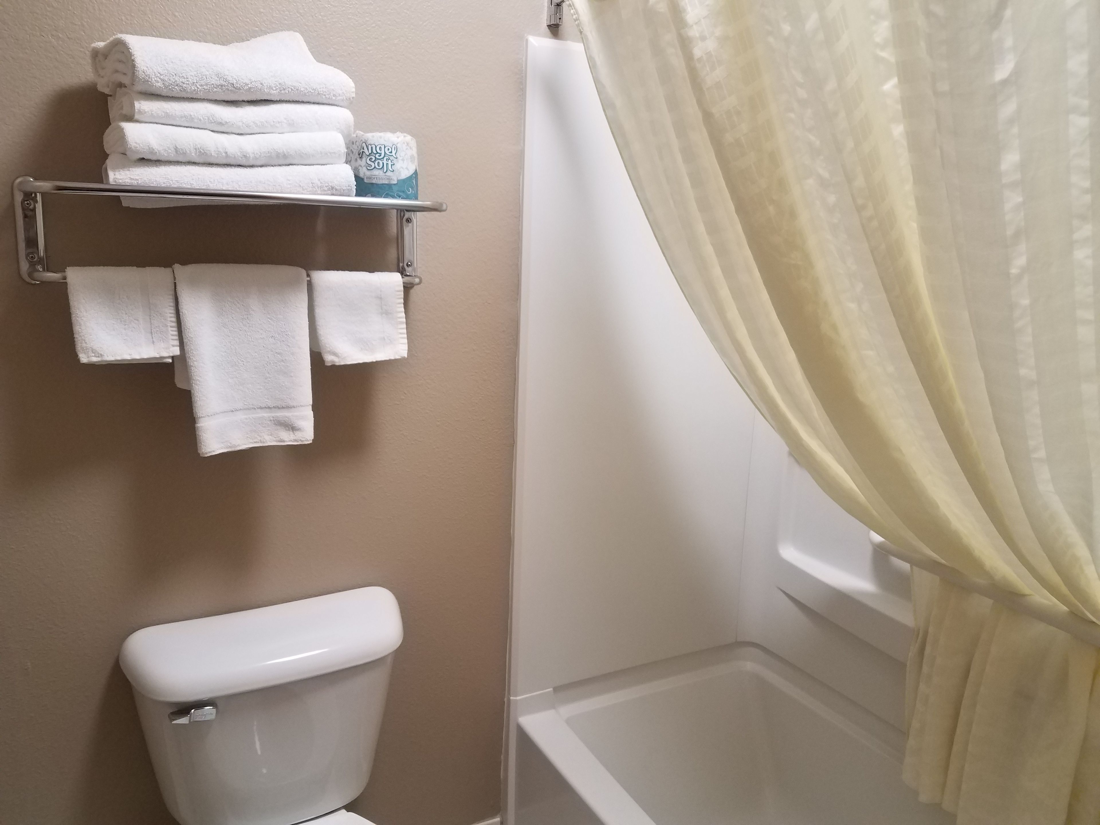 A bathroom with a toilet, a shelf with folded towels, and a shower curtain.