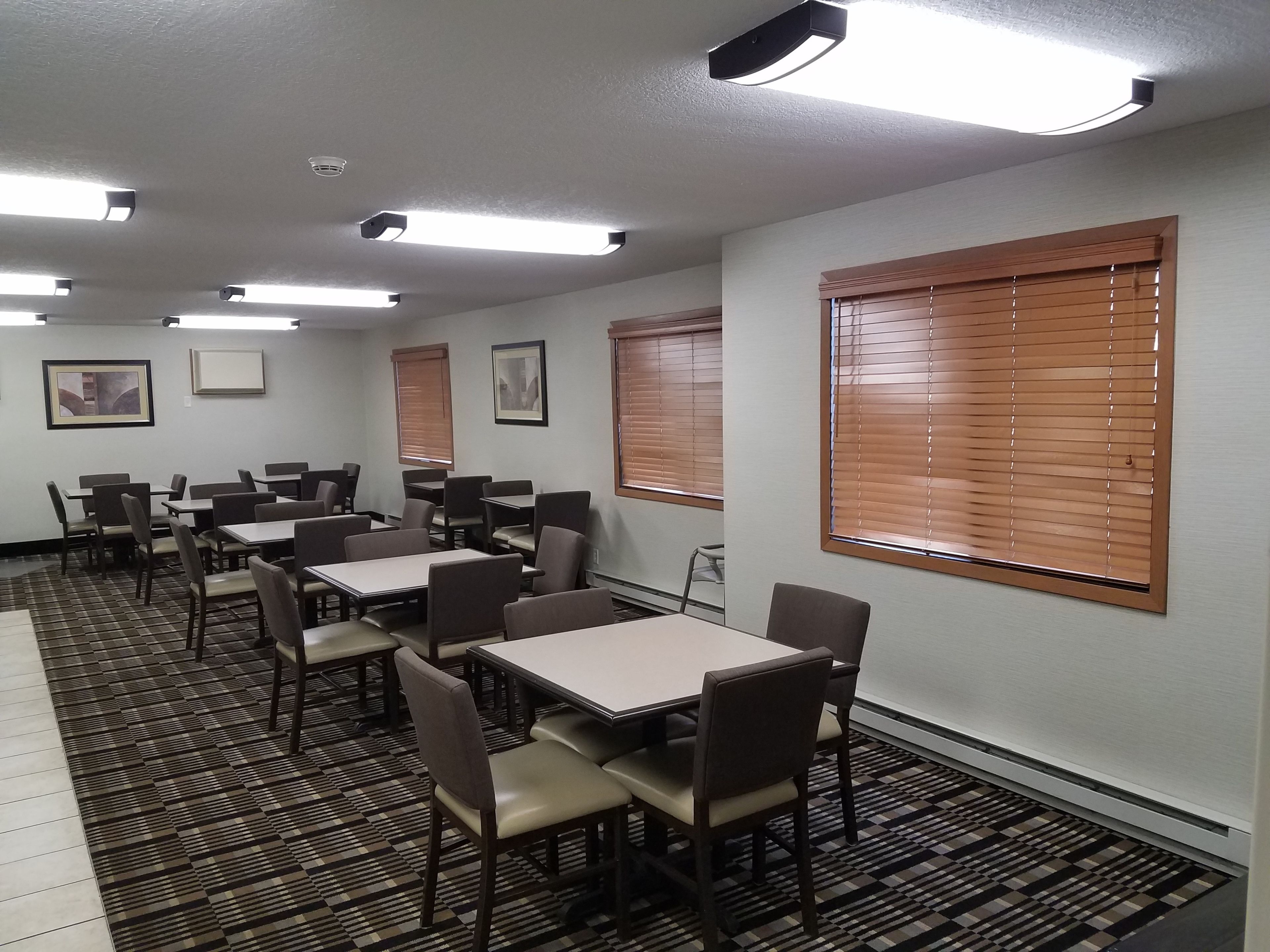 A conference room with tables and chairs, large windows with blinds, and ceiling lights.