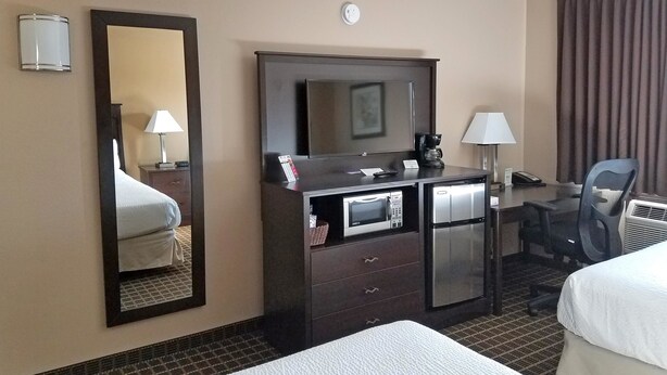 A hotel room with a bed, a desk with a computer, a mirror, a coffee maker, and a chair. - Americas Best Value Inn & Suites Bismarck (Bismarck)