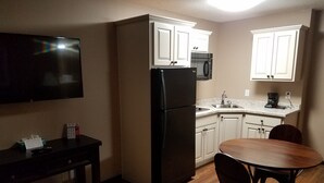 A compact kitchen with white cabinets, a black refrigerator, a microwave, a coffee maker, and a dining table with chairs. - Americas Best Value Inn & Suites Bismarck (Bismarck)