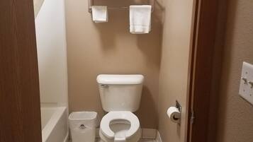 A small bathroom with a toilet, a toilet paper holder, a towel rack with folded towels, a trash bin, and a shower curtain.