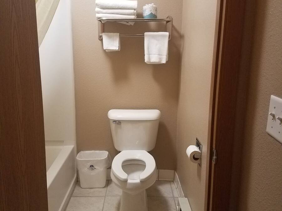 A small bathroom with a toilet, a toilet paper holder, a towel rack with folded towels, a trash bin, and a shower curtain.
