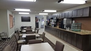 A hotel dining area with tables and chairs, a kitchen counter with appliances, and a television on the wall. - Americas Best Value Inn & Suites Bismarck (Bismarck)