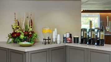 Ein Frühstücksbuffet mit Blumenarrangements, einer Punschschüssel, gestapelten weißen Tassen und Kaffeeautomaten.