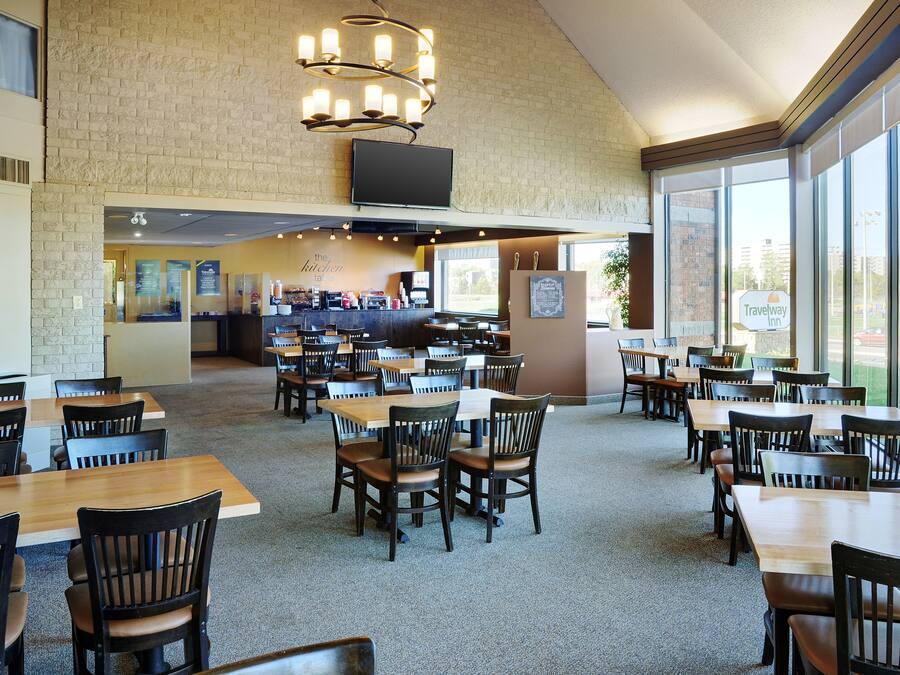 A spacious dining area with multiple tables and chairs, a brick wall, and a large window providing natural light.