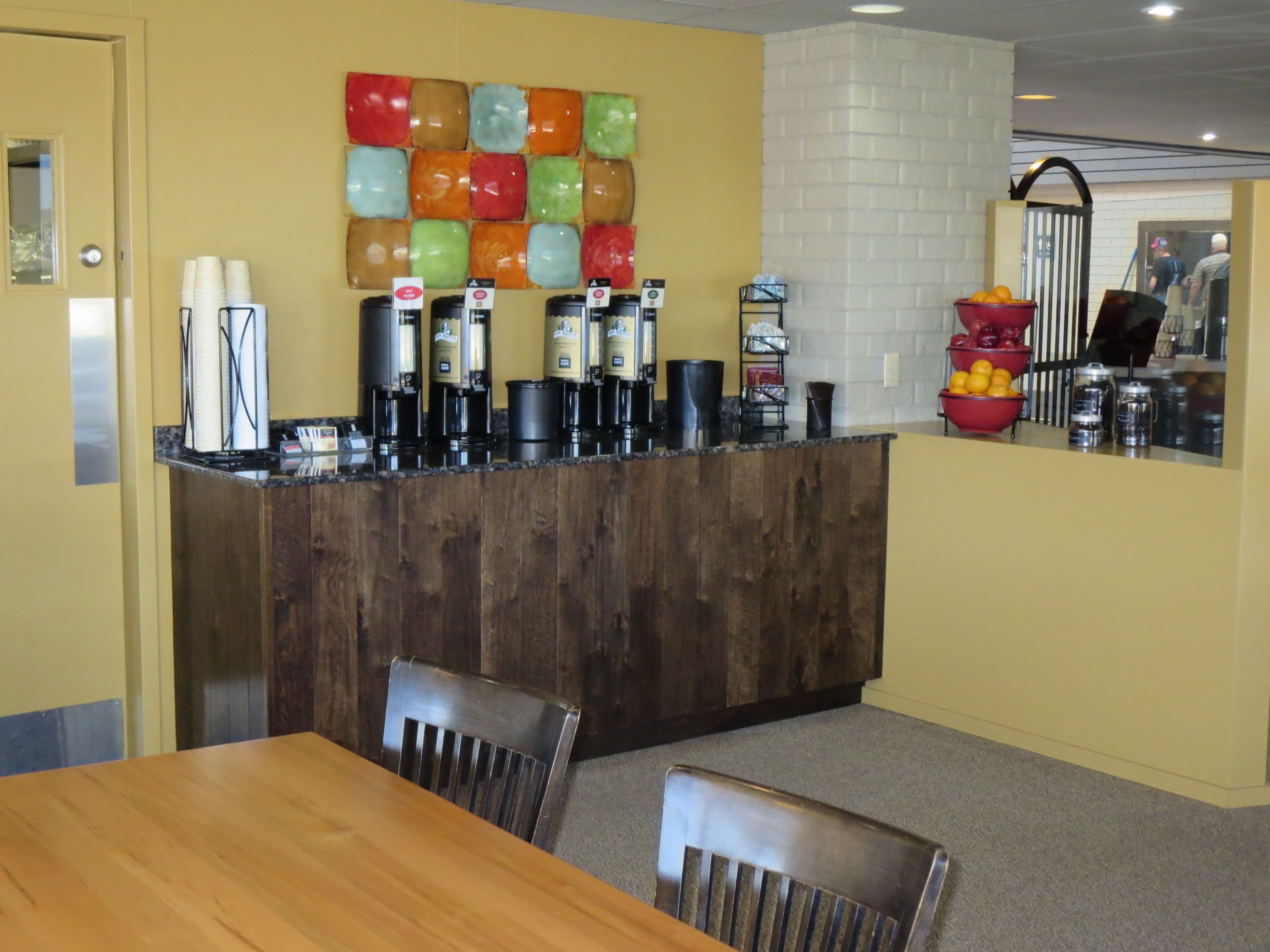 Un espace bar doté d’un comptoir en bois, de plusieurs distributeurs de café et d’une décoration murale colorée.