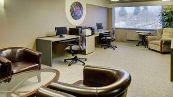 A conference room with a large clock, multiple computer stations, leather chairs, and a large window with a view of trees.