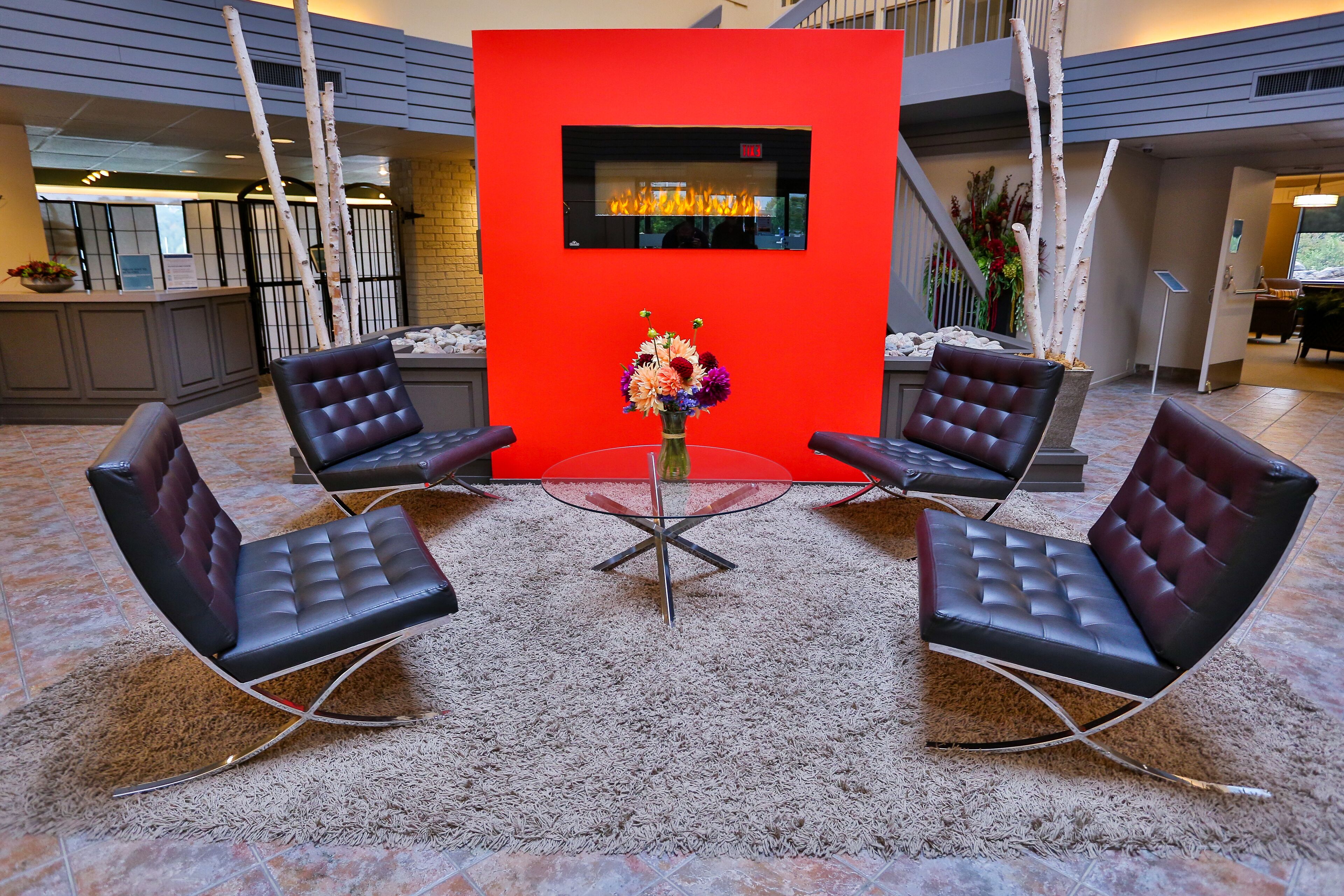 A lobby with four leather chairs around a glass table, a red accent wall, and a fireplace.