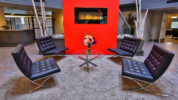 Un hall con cuatro sillones de cuero alrededor de una mesa de vidrio, una pared decorada en rojo y una chimenea.