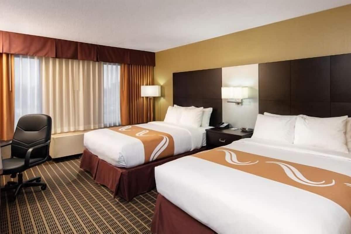 A hotel room with two beds, a desk, a chair, and a large window with curtains.