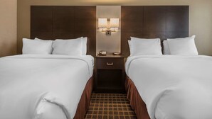 Habitación de hotel con dos camas, una mesita de noche con lámpara y un cajón pequeño.
