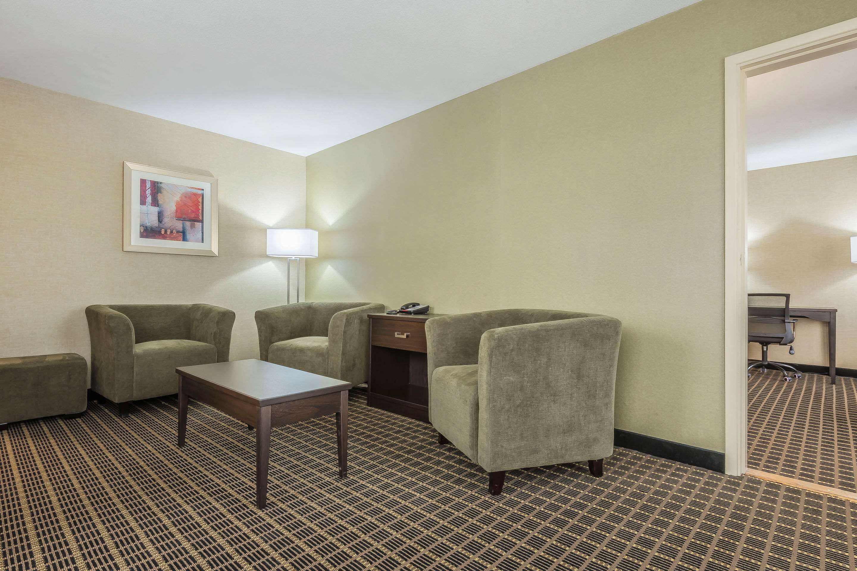 Une chambre d’hôtel avec une moquette à motifs, quatre fauteuils, une petite table, une lampe et un tableau encadré au mur.
