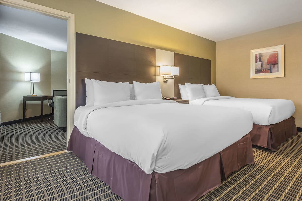 A hotel room with two beds, a nightstand, a lamp, and a painting on the wall.