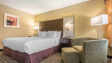 A hotel room with a large bed, a bedside table with a lamp, a chair, and a patterned carpet.