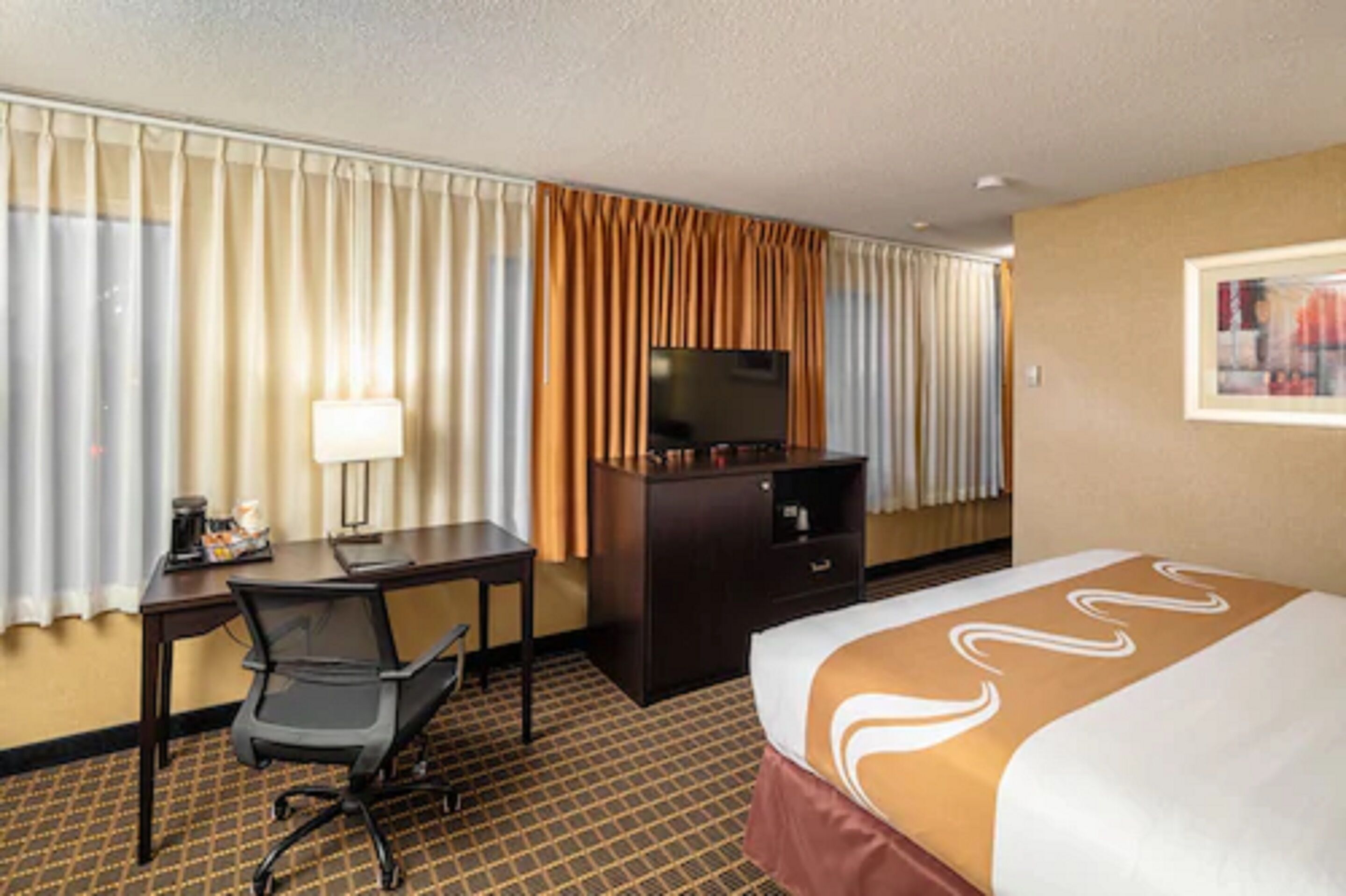 Una habitación de hotel con cama, escritorio, silla, televisor y cómoda.
