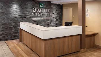 Balcão de recepção com parede de pedra ao fundo e placa com a inscrição "Quality Inn & Suites by Choice Hotels".