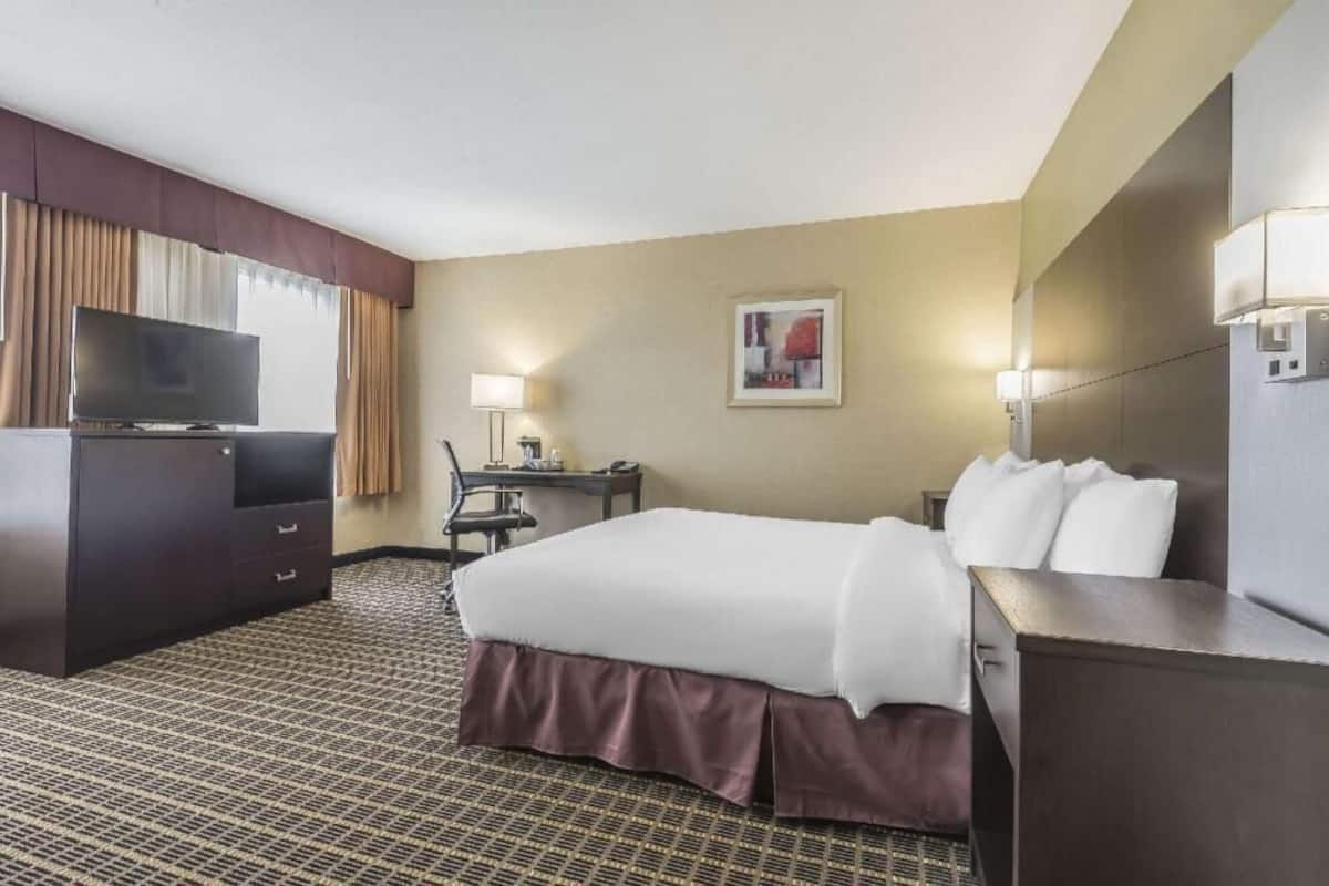 A hotel room with a bed, a desk, a television, and a lamp.