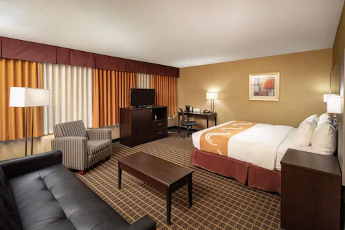 Una habitación de hotel con cama, sofá, escritorio con ordenador, televisor y lámpara.