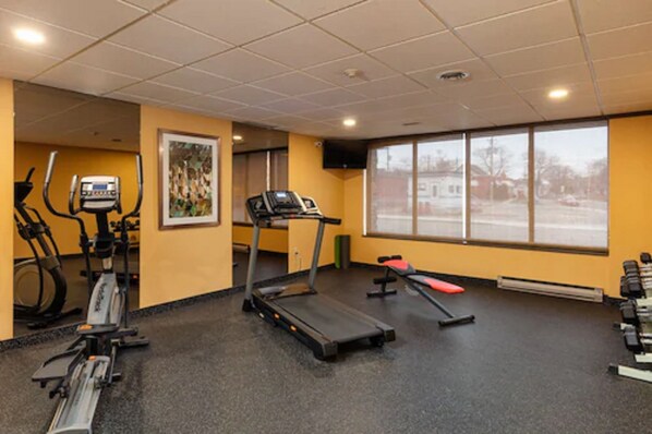 Une salle de sport équipée de tapis de course, de vélos elliptiques et d’un banc rouge.