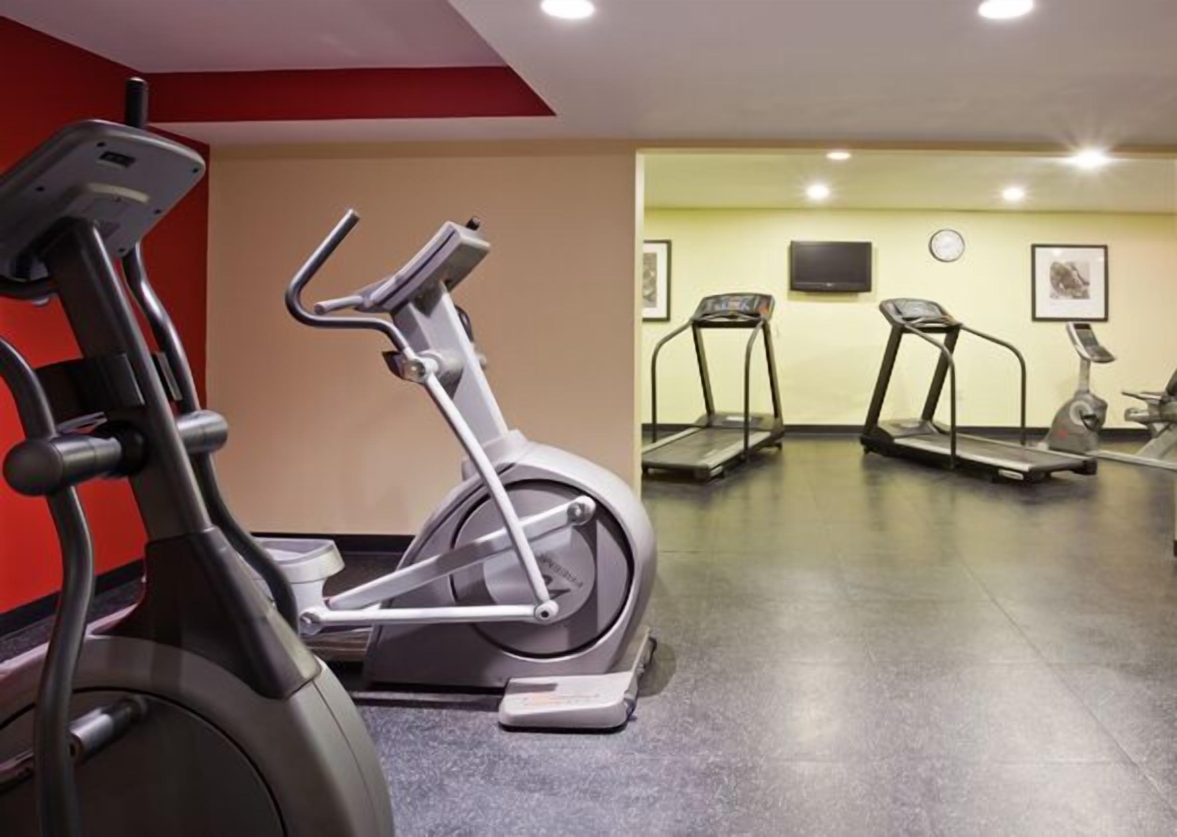 Un gimnasio con bicicletas estáticas, cintas de correr y un televisor montado en la pared.