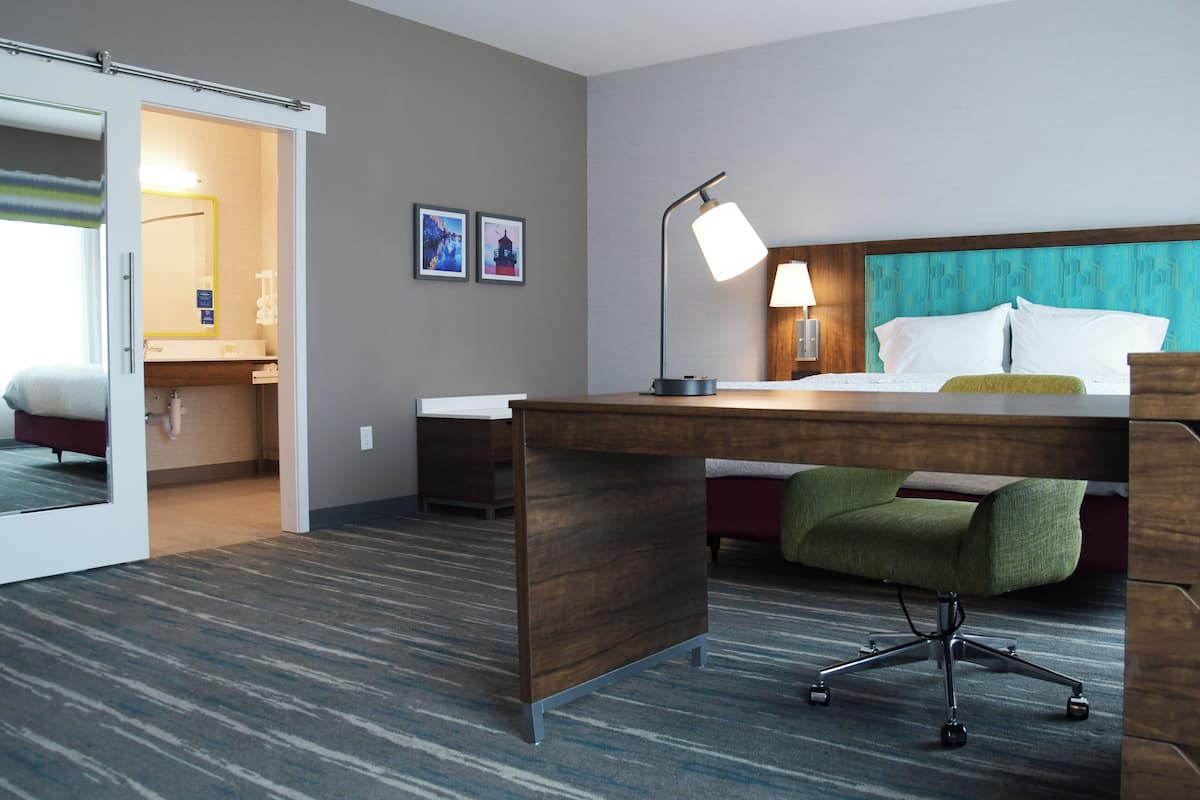 A hotel room with a bed, desk, chair, and a bathroom visible through an open door.