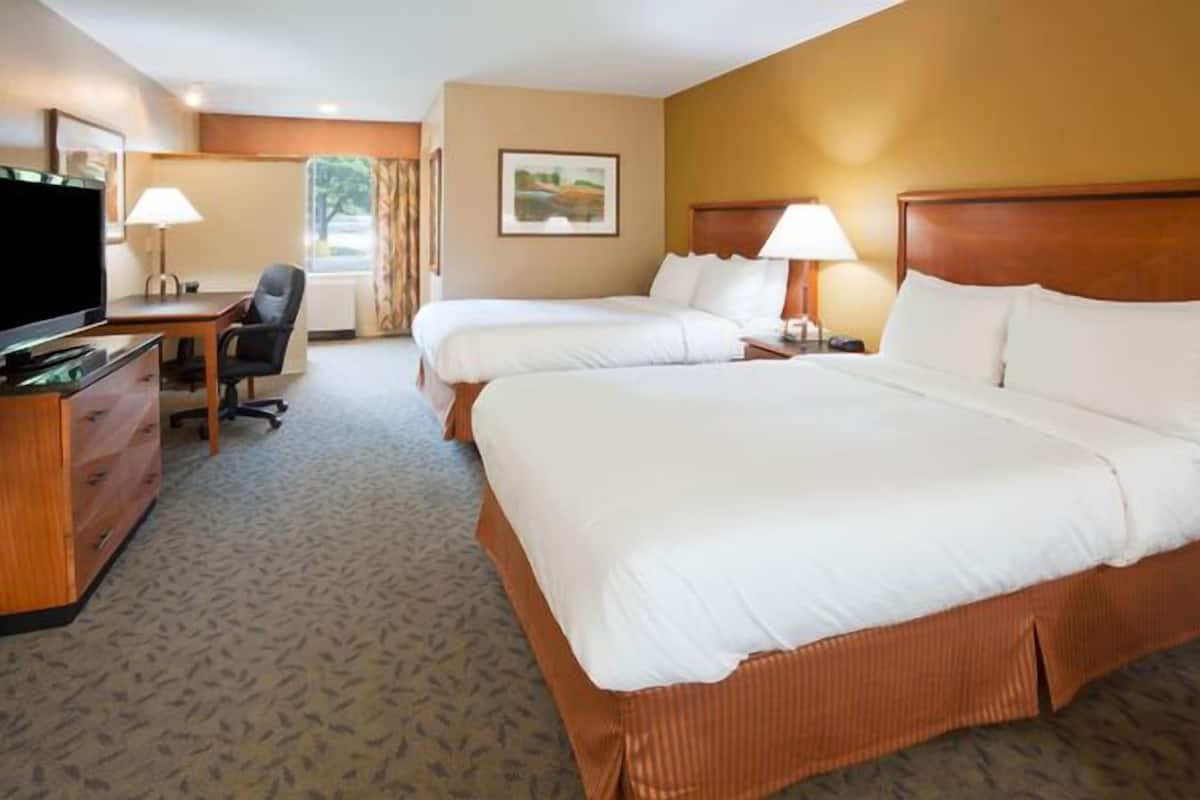 A hotel room with two beds, a desk, a television, and a window with curtains.