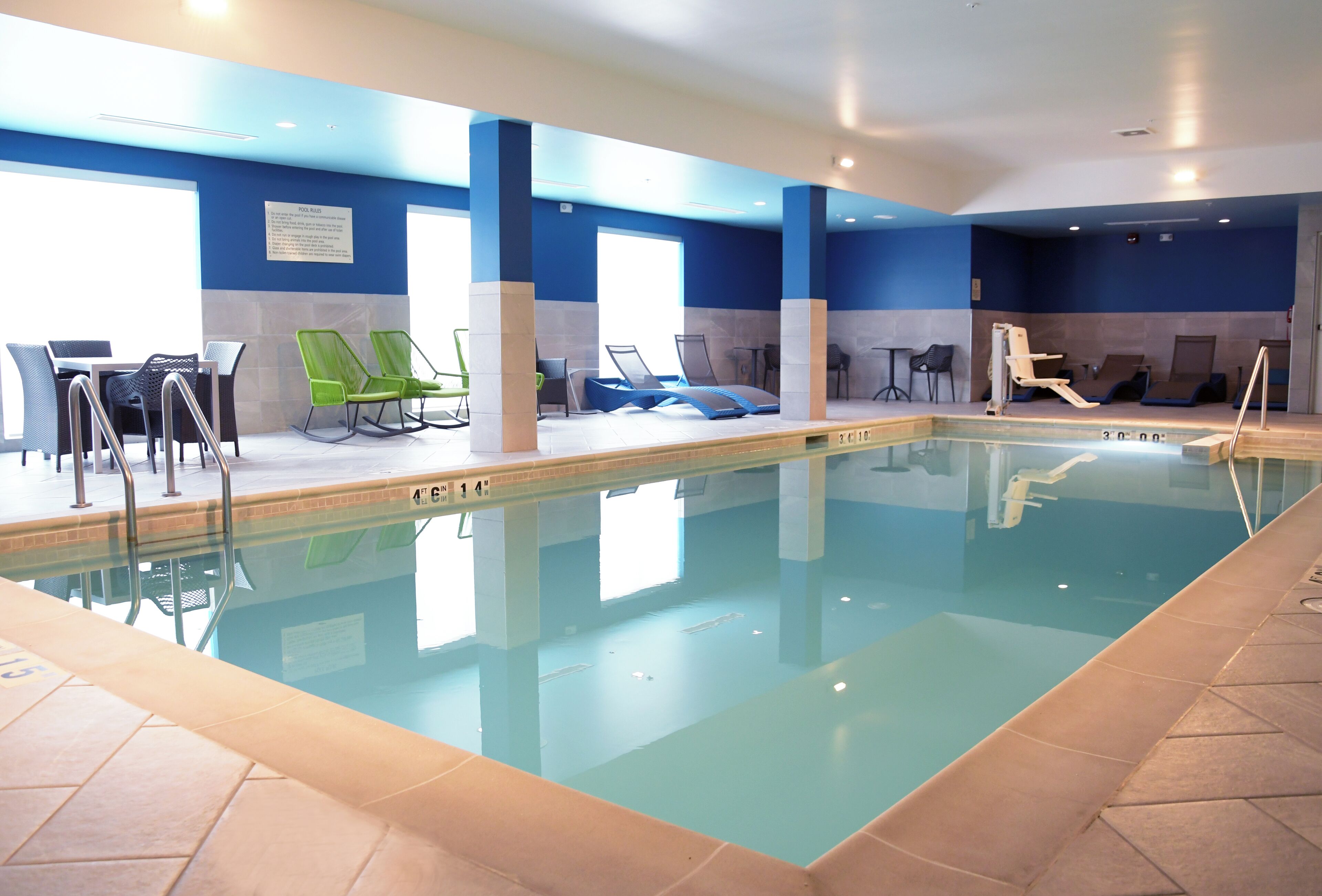 An indoor swimming pool with lounge chairs and a seating area.