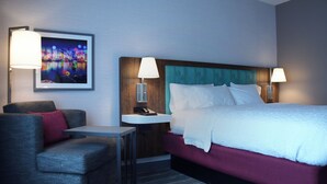 A hotel room with a bed, a chair, a desk, and a nightstand with a lamp. - Hampton Inn Glendale Milwaukee, WI (Milwaukee)