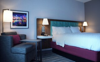 Una habitación de hotel con una cama, una silla, un escritorio y una mesita de noche con lámpara.