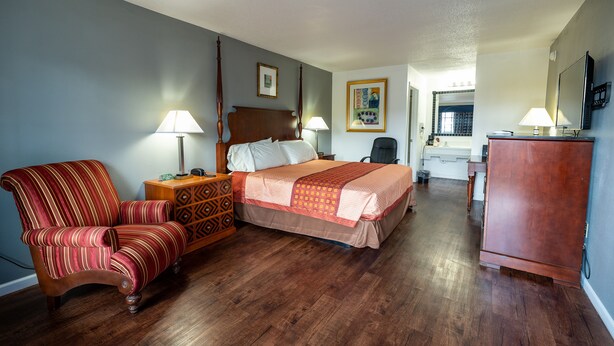 Una habitación de hotel con cama, sillón, escritorio y cómoda.