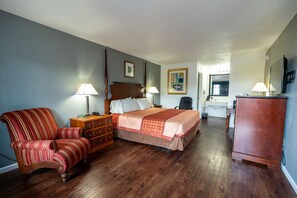A hotel room with a bed, a chair, a desk, and a dresser. - American Inn & Suites Russellville (Russellville)