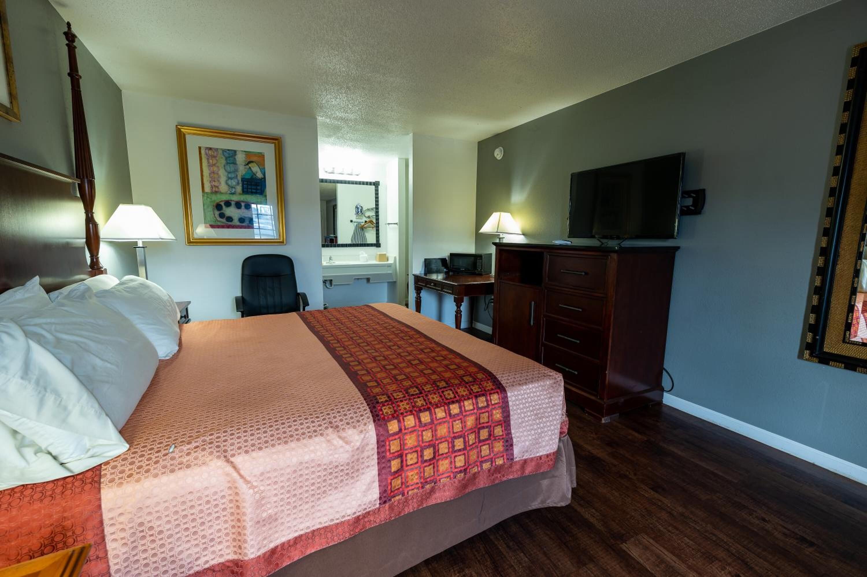 Una habitación de hotel con una cama, un escritorio, una silla, un televisor y un espejo.