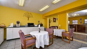 Un comedor con paredes amarillas, mesas blancas y sillas de madera.