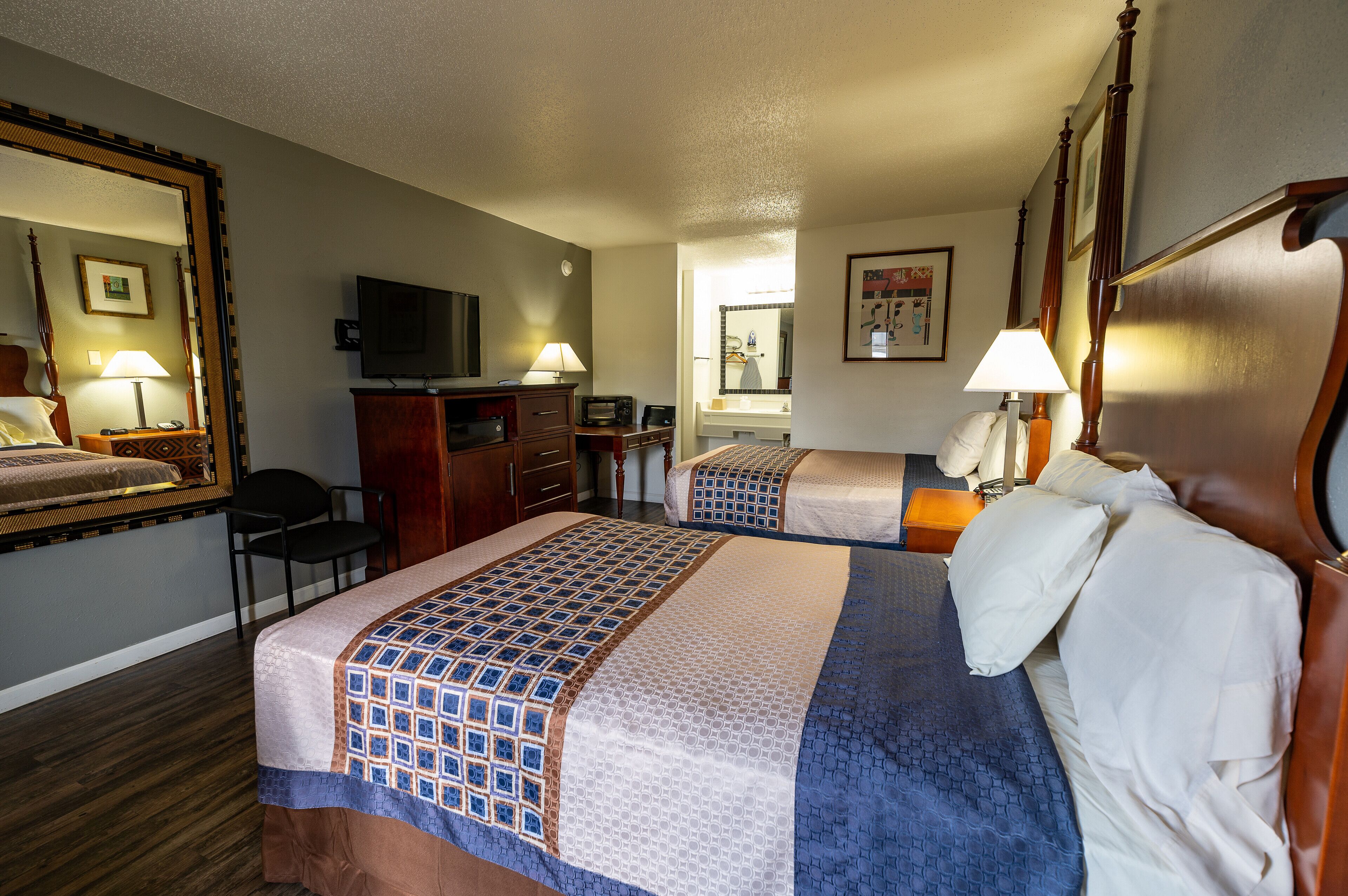 A hotel room with two beds, a desk, a chair, a television, and a mirror.