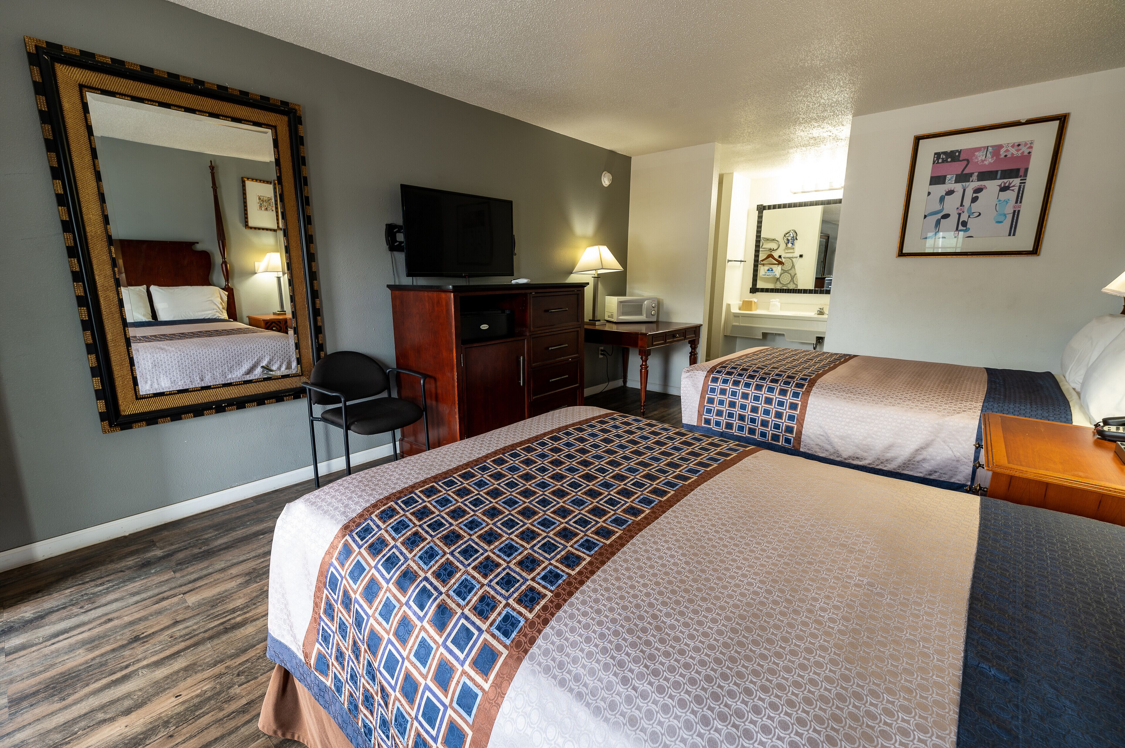 A hotel room with two beds, a desk, a chair, a television, a mirror, and a framed picture on the wall.
