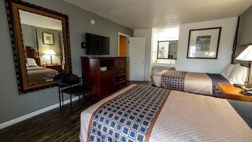 Habitación de hotel con dos camas, un escritorio, una silla, un aparador, un televisor y un baño visible a través de una puerta abierta.