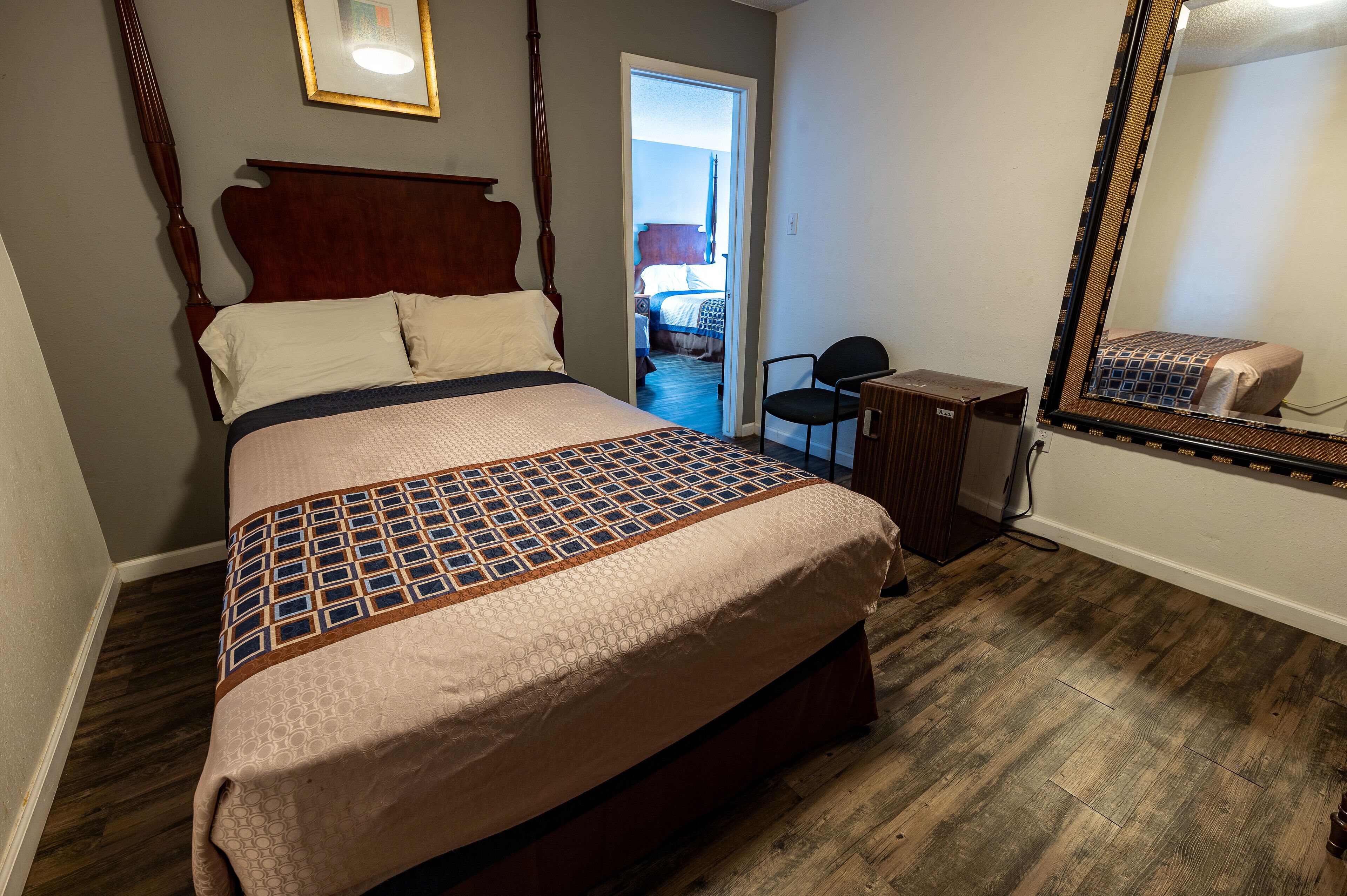A bedroom with a four-poster bed, a wooden desk, and a mirror.