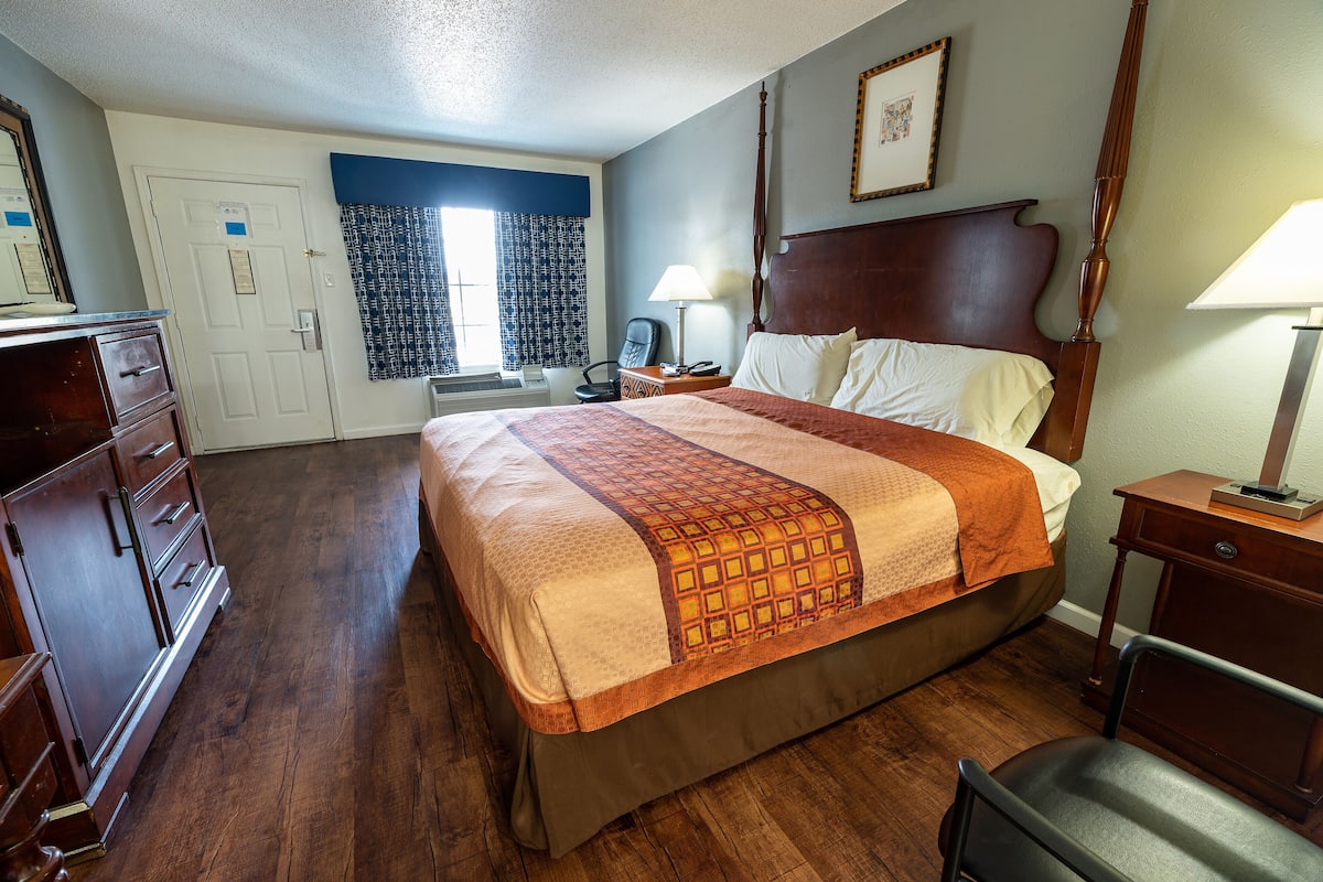 A hotel room with a large bed, wooden dresser, and a desk with a lamp.